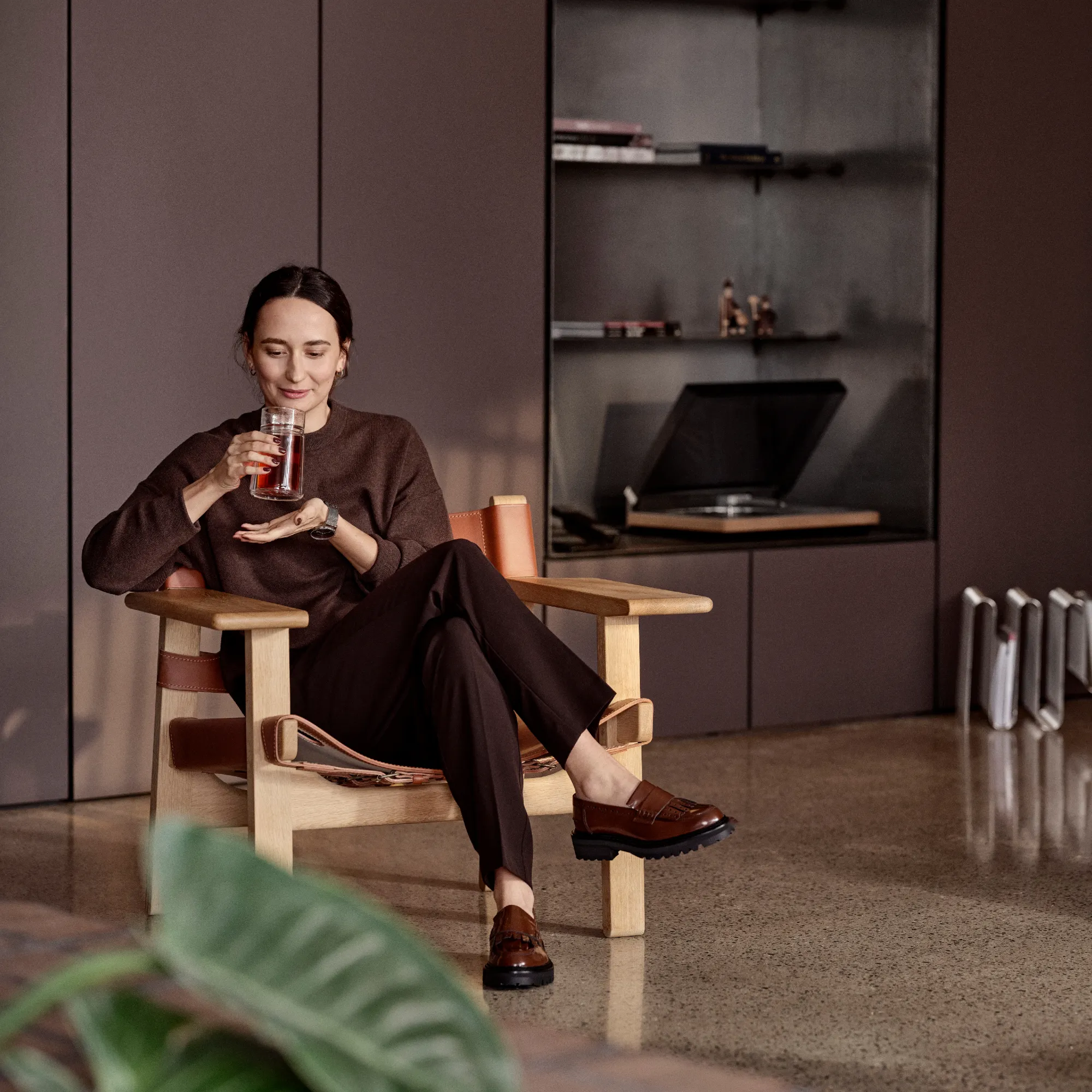image kobieta, fotel drewniany, brązowy sweter, czarne spodnie, mokasyny brązowe