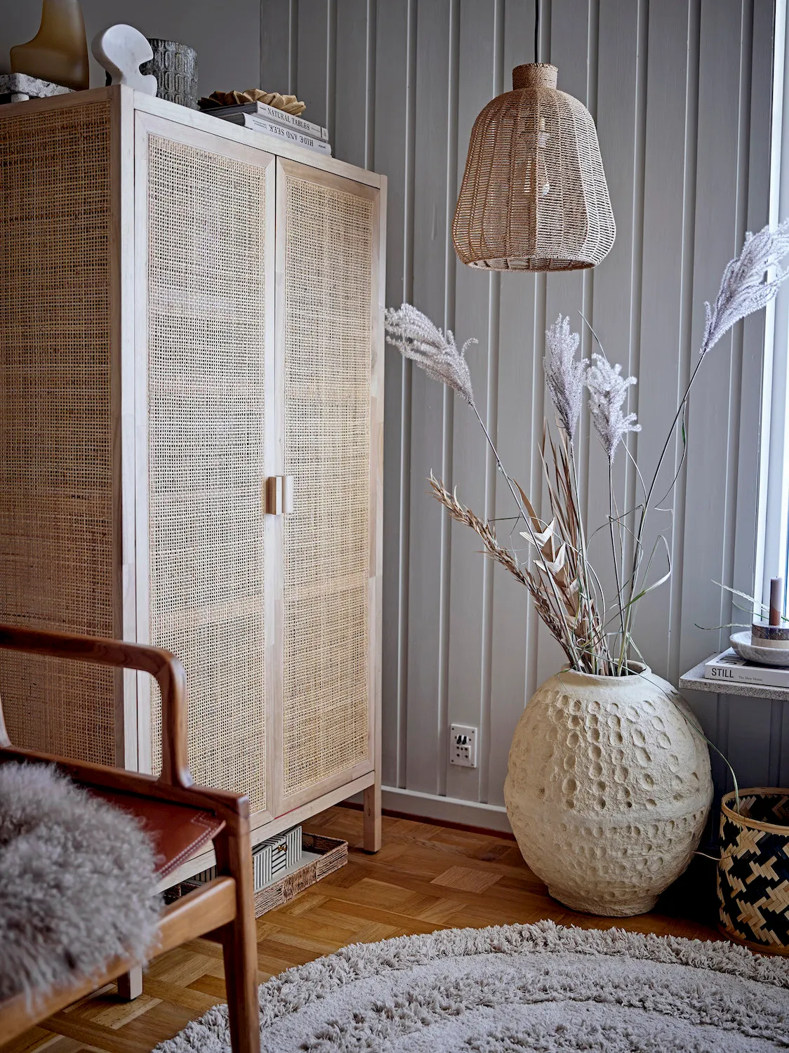 image szafa z plecionką, duża doniczka, lampa rattanowa, dywan z wełny, kwietnik w stylu skandynawskim